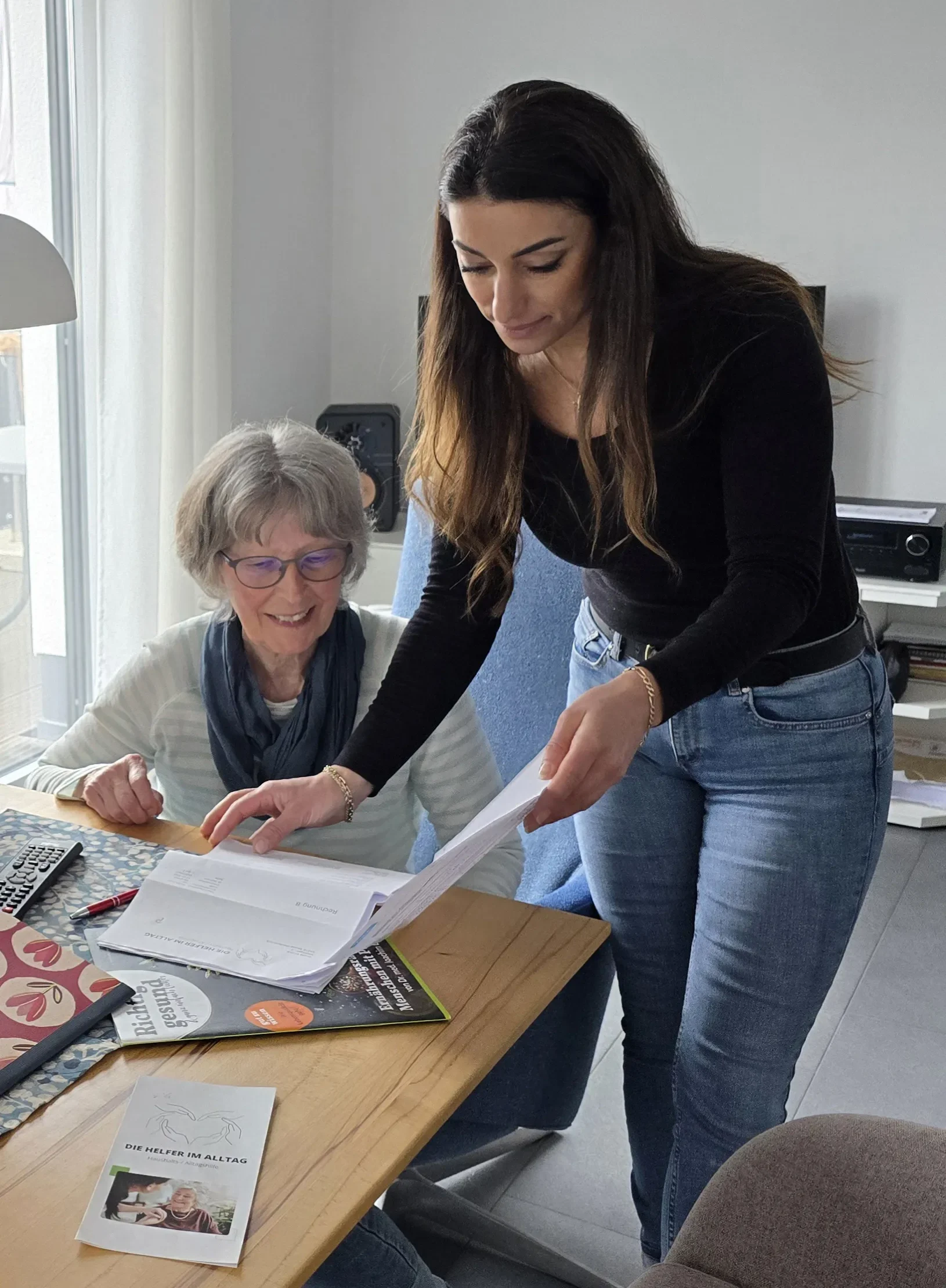 Inhaberin von Die Helfer im Alltag und eine fröhliche Seniorin am Tisch.